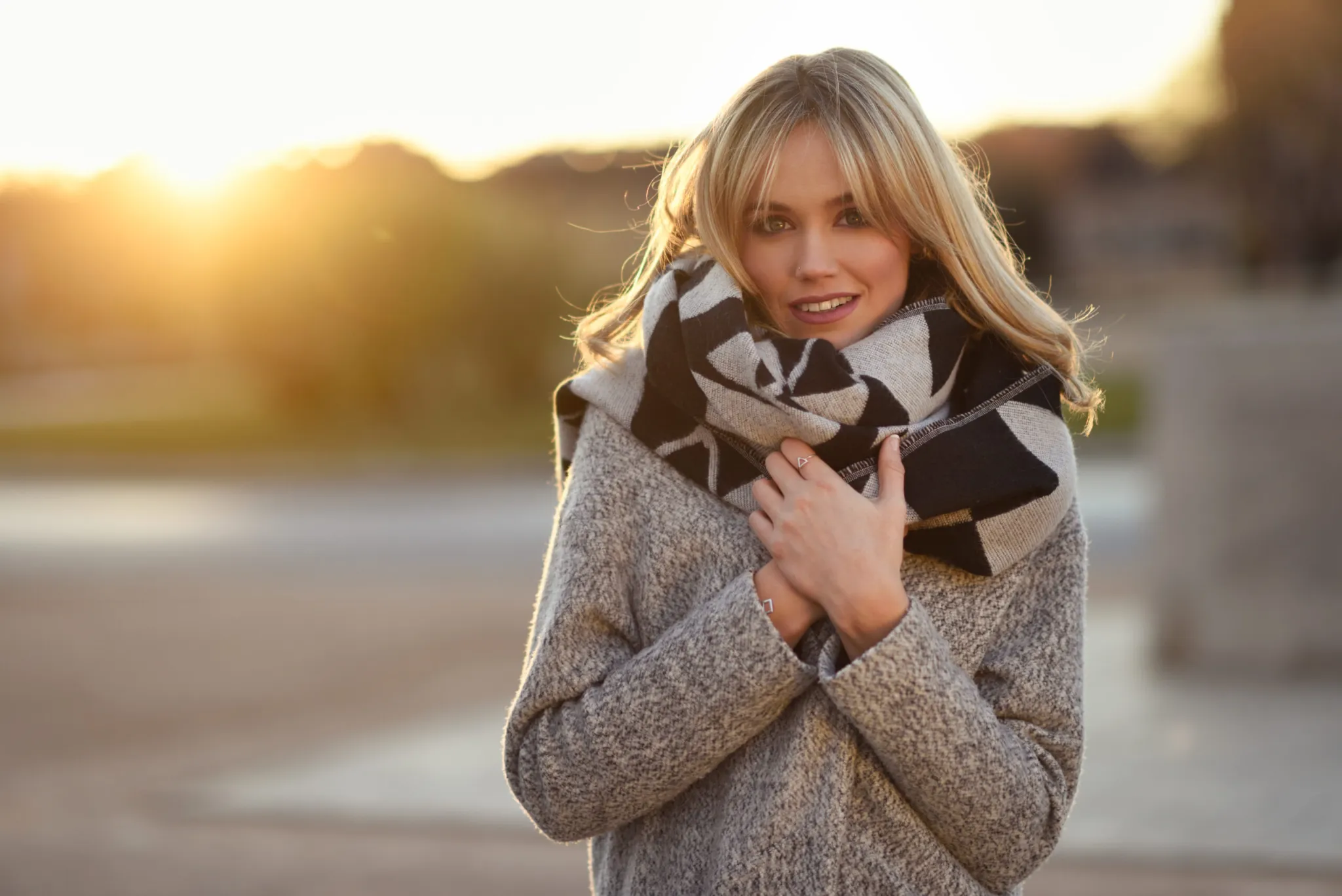 Beautiful young blonde woman in urban background Attractive blonde woman in urban background with sun backlight Young girl wearing winter coat and scarf standing in the street Pretty female with straight hair hairstyle and blue eyes | Walnut Creek Aesthetics in Walnut Creek, CA