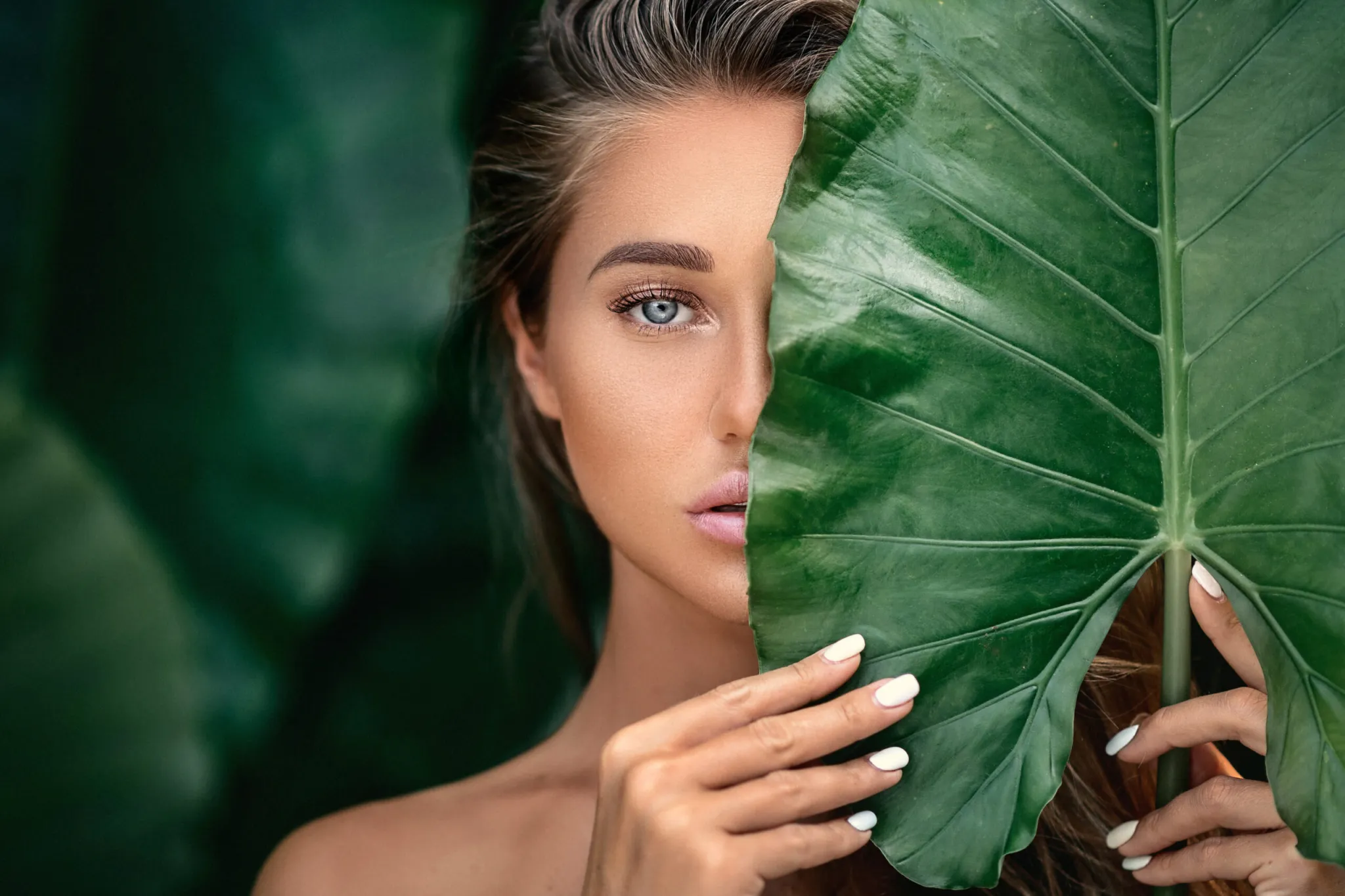 Young woman with a smooth skin holding monstera deliciosa plant leaf | Walnut Creek Aesthetics in Walnut Creek, CA